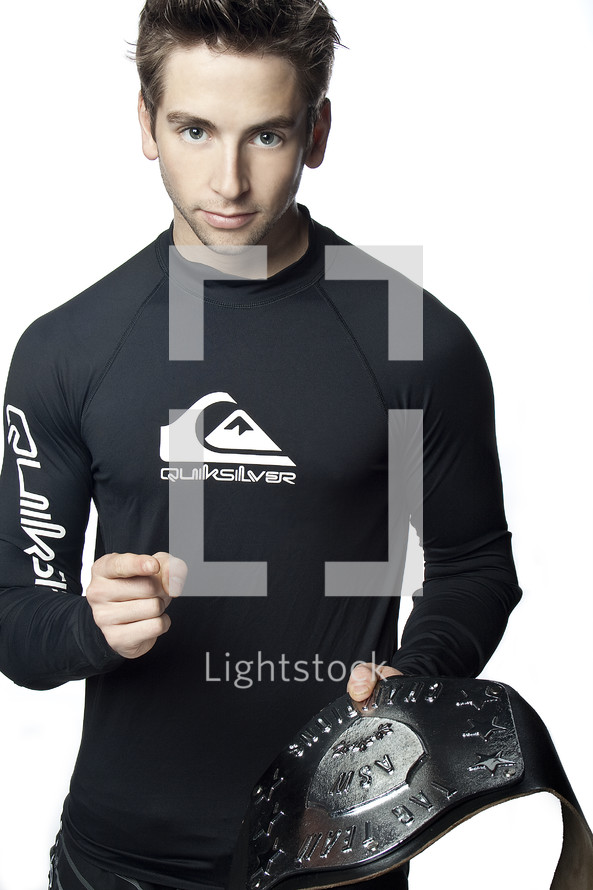 Champion; man in black rash guard holding a championship belt, pointing towards the camera.