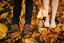 feet of a couple lying in a pile of leaves 