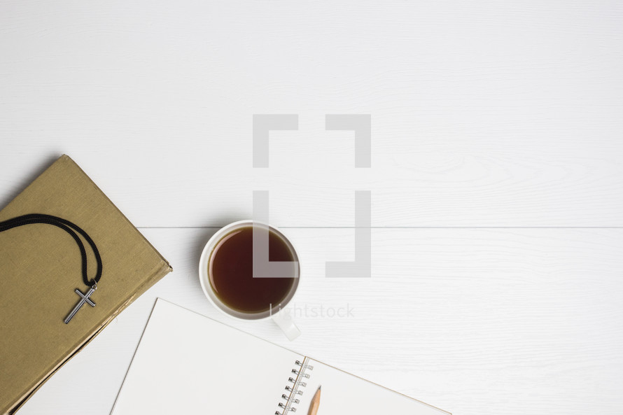 cross necklace, coffee cup, pencil and notebooks on a white background 