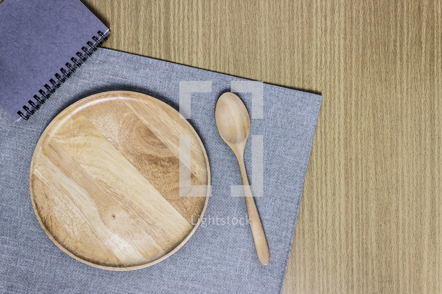 wooden plate, spoon, placemat, and notebook on a table 