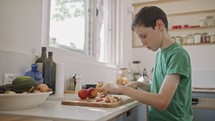 Young boy working in the kitchen slicing fruit for breakfast