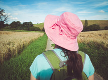 woman in a pink sunhat and backpack hiking through a field