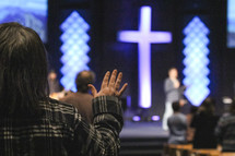 raised hand during a worship service with a glowing cross in the background 