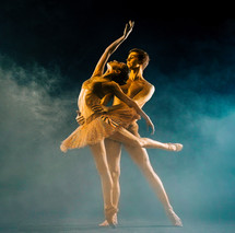 Professional, emotional ballet dancers on dark scene performed by golden couple with body-art. Shining gold skin. Pair depicts love and passion on stage in smoke