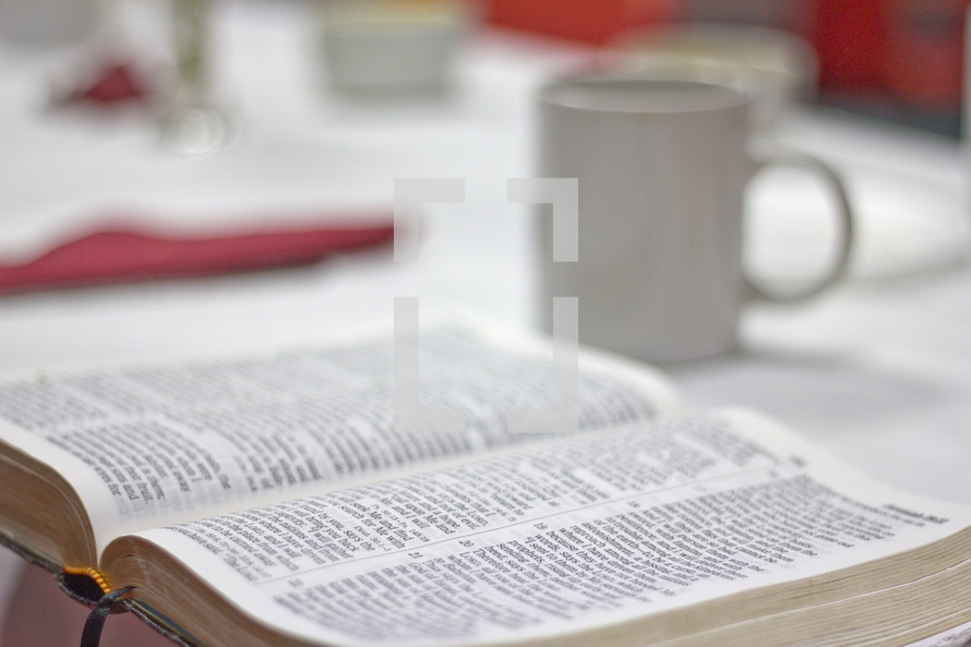 Open Bible on a table and a coffee mug 