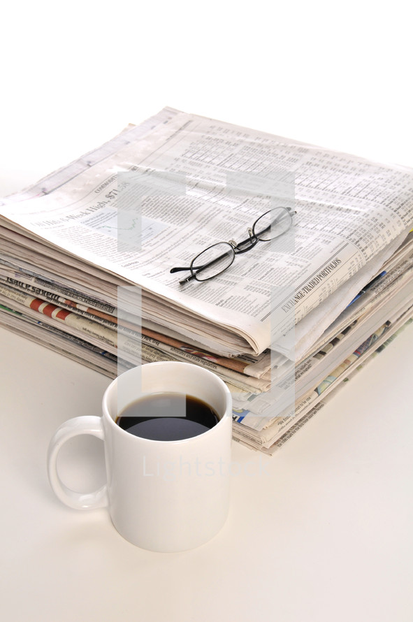 stack of newspapers, coffee mug, and reading glasses 