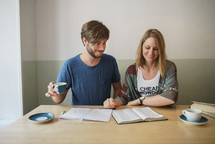 a man and woman sitting at a table with a Bible and journal 