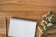 pencil, notepad, and flowers on a wood table 