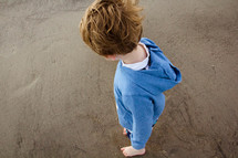 a boy child standing barefoot on a beach 