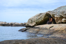 a woman reading a Bible on a rocky shore 