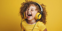 Joyful little girl with curly hair enjoying music with yellow headphones against a vibrant yellow background.
