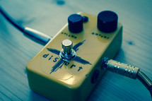 A guitar distortion effect pedal with cables plugged in to each side.