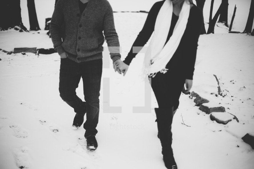 couple holding hands walking through snow 