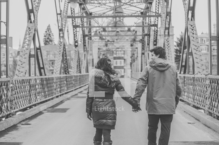 a couple holding hands walking across a bridge 
