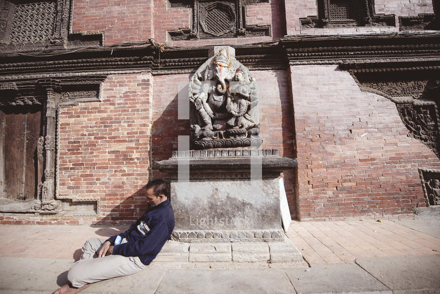 man sleeping leaning against a statue 