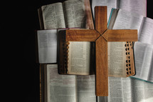wooden cross on a pile of open Bibles 