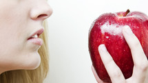 Woman (Eve) holding a red apple in front of her mouth.