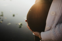 a pregnant silhouette against a sun setting on the lake 