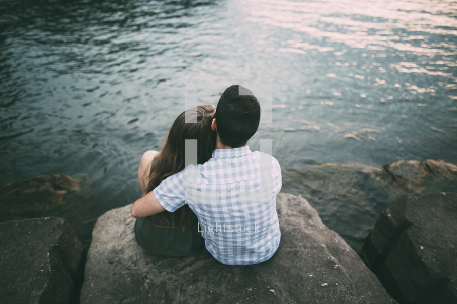 couple hugging sitting on rocks by a lake 
