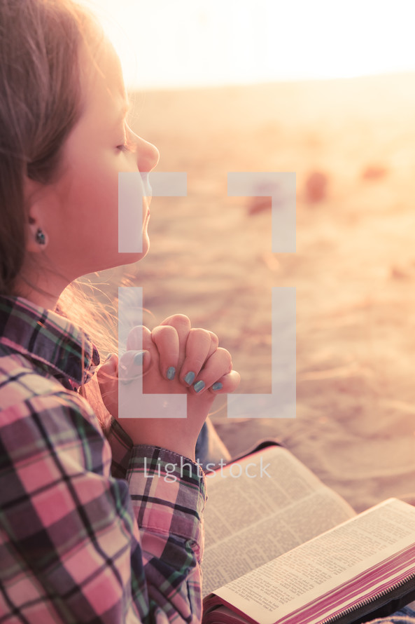 young girl praying on the beach with her bible in her lap at sunset; thinking, hearing from God