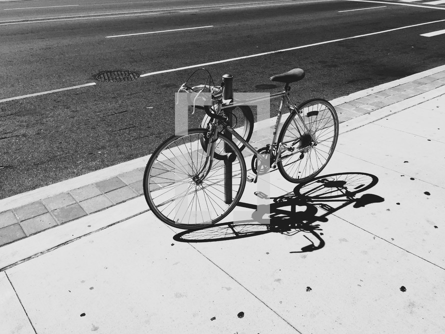 A bicycle chained to a pole on a city sidewalk.