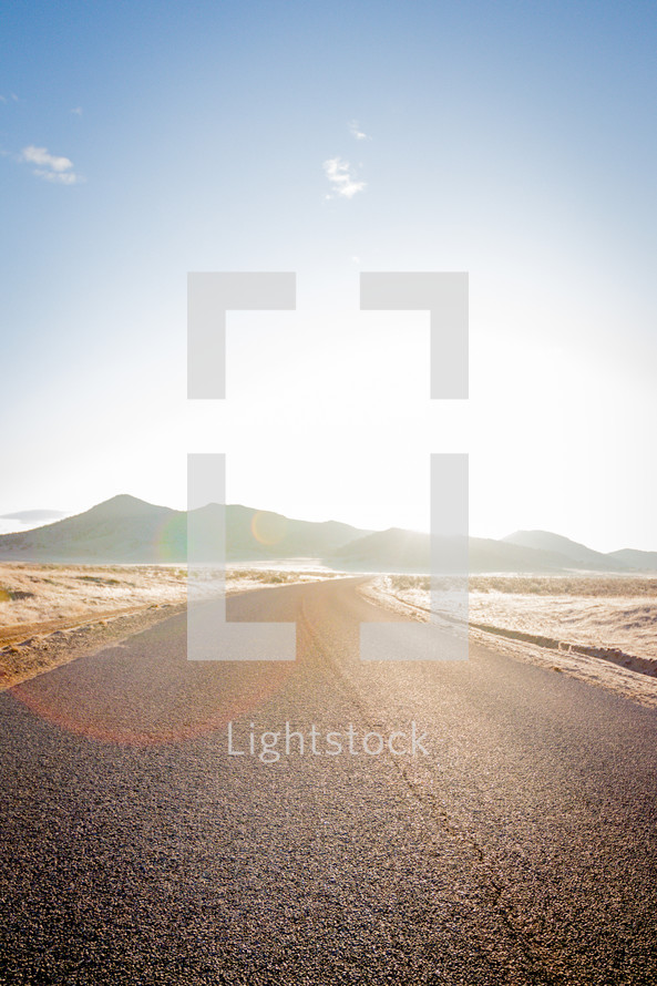 paved road under bright sunlight through a desert 