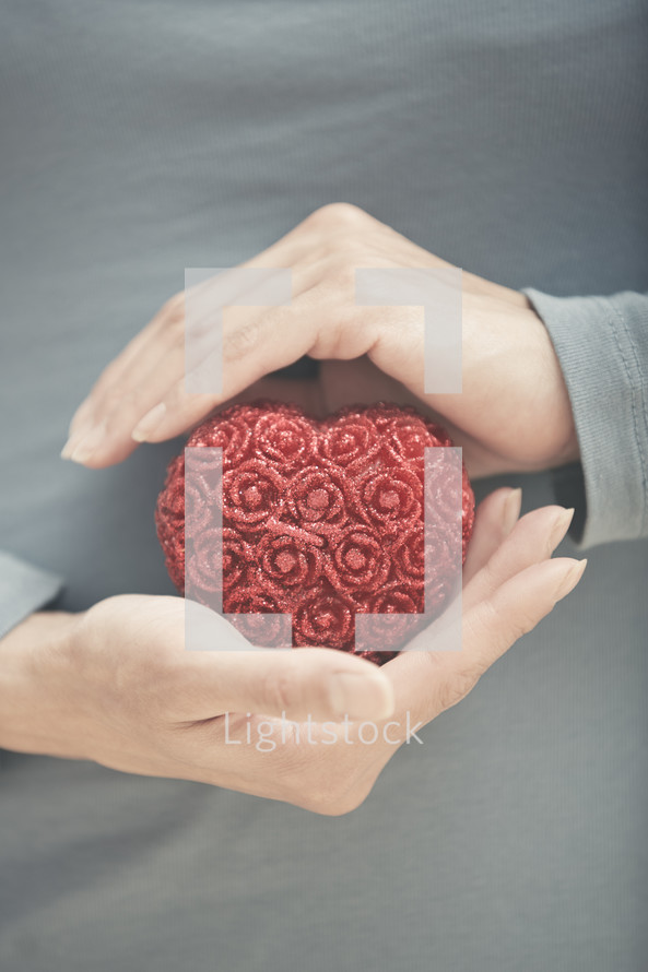cupped hands holding a red heart 