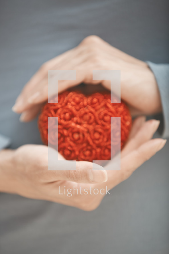 cupped hands holding a red heart 