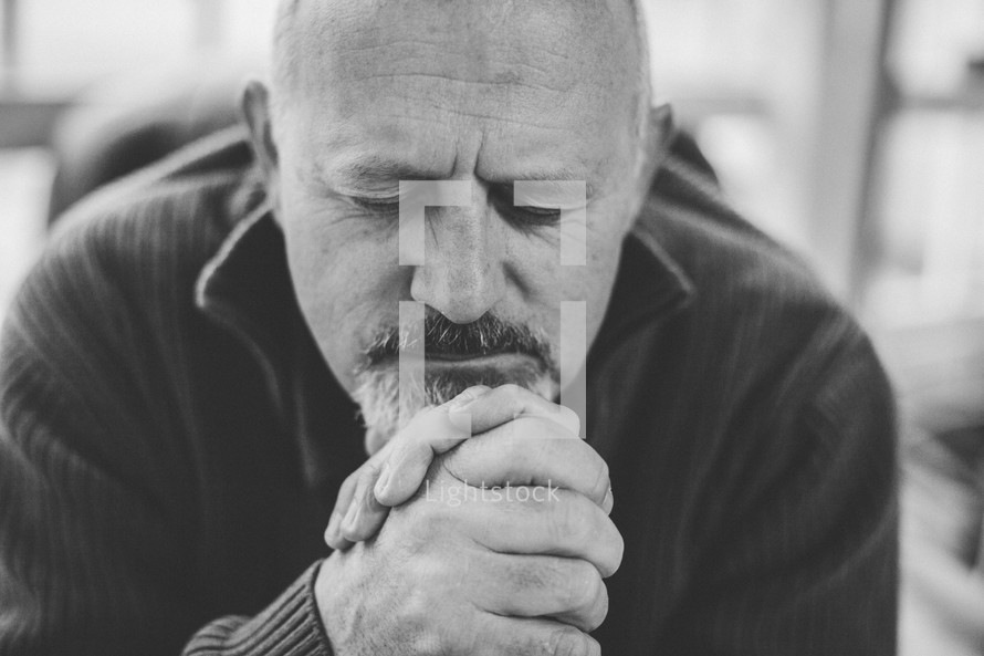 Man praying with his head on his hands.