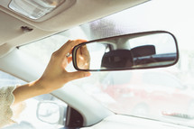 a woman adjusting a rearview mirror 