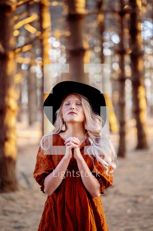 a woman standing in a forest alone praying 