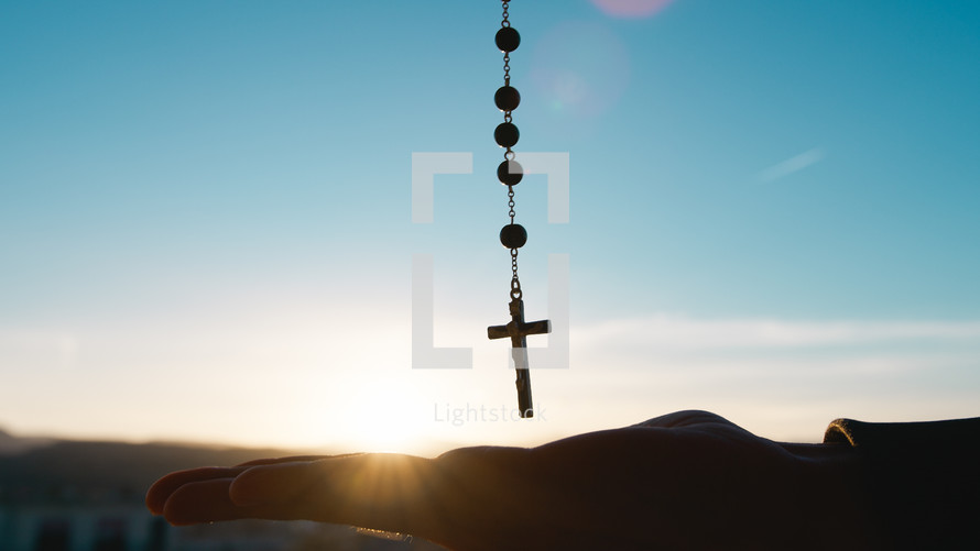 Silhouette of crucifix with sky background and hand on the bottom