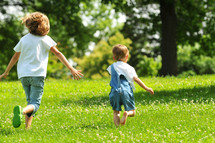 Sister chasing her brother through a grassy field.