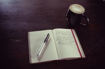 pen on the pages of a journal and a coffee mug 