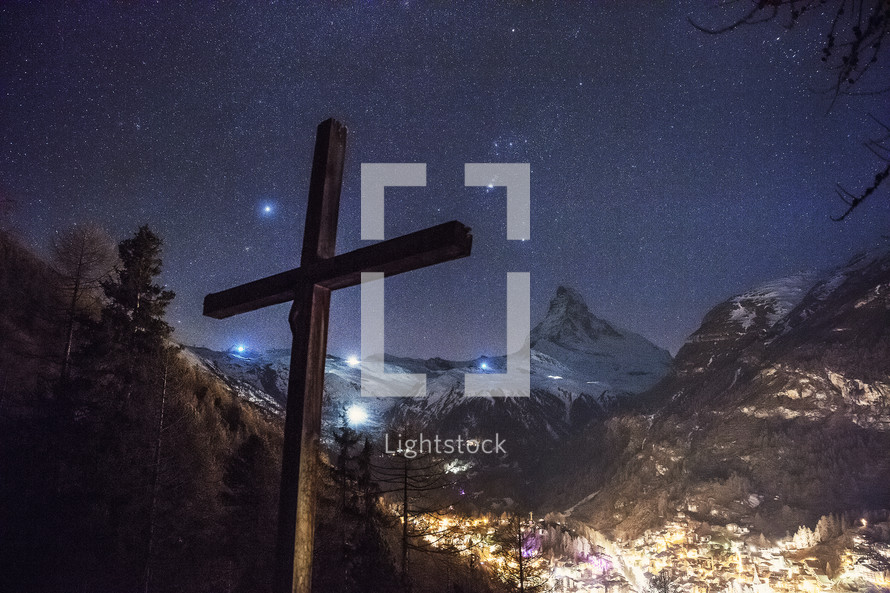 cross and view of glowing lights in a valley 