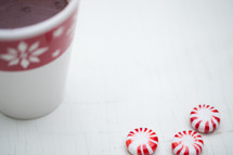 Peppermint candies and a cup of hot chocolate in a Christmas cup on a white table.