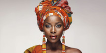 Elegant African woman in traditional headwrap with vibrant orange patterns and matching beaded earrings.