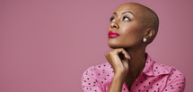 Thoughtful woman with bald head, wearing pink polka dot blouse.
