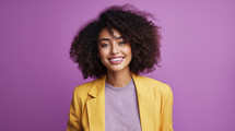 Vivacious young woman with curly hair wearing a yellow blazer over a lilac top, against a purple background.