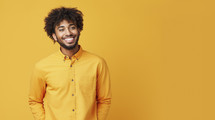 Portrait of a cheerful young man with afro hair, wearing a bright yellow shirt against a matching yellow background.