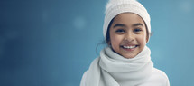 Smiling young girl in winter hat and scarf against blue background.