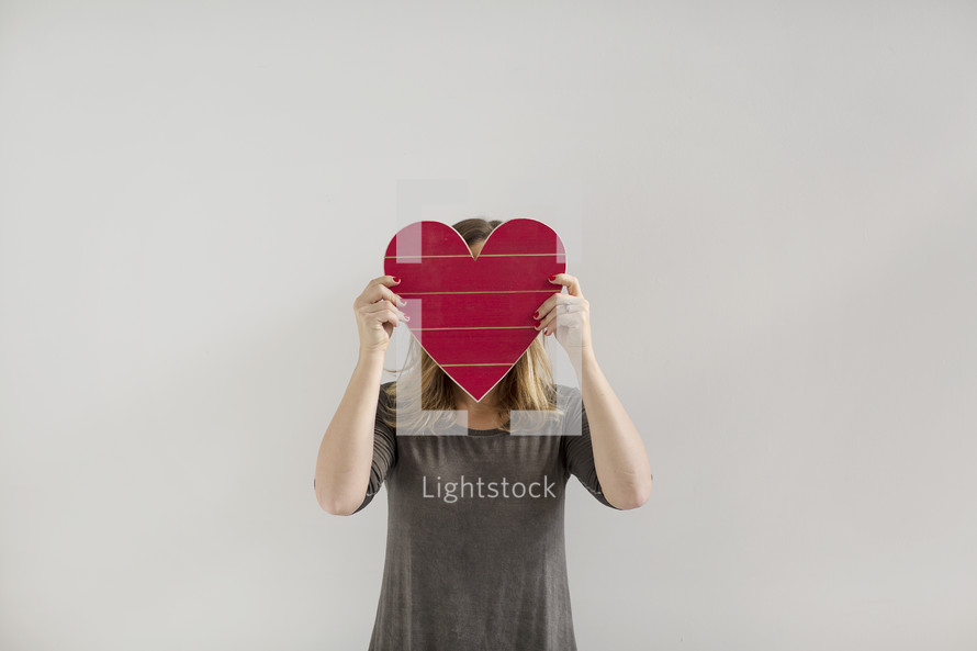 a woman covering her face with a red wooden heart 