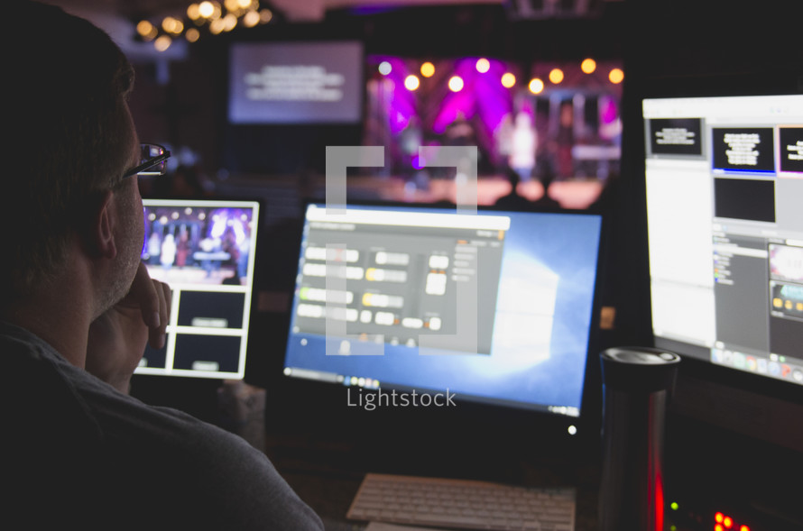 a man watches a worship service while running the media boards. 