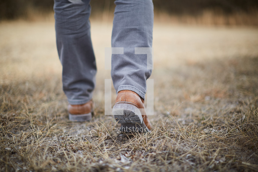 feet of a man walking in grass 