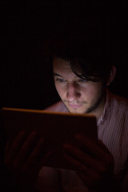 A man illuminated by the light from an electronic tablet.