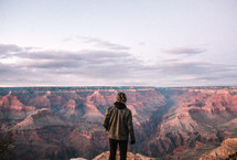 a man standing at the edge of a cliff looking out at canyons 