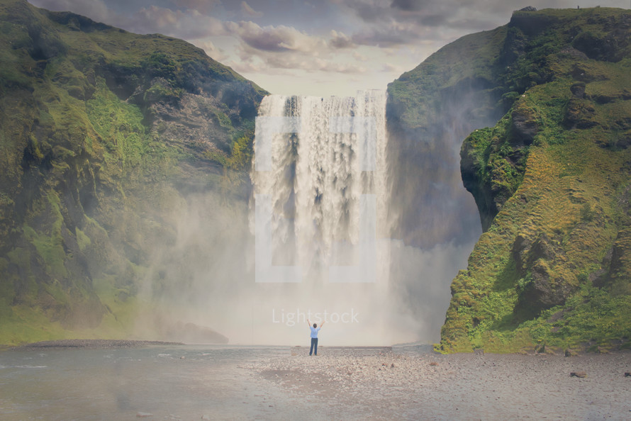 a person standing in front of a waterfall with raised arms 