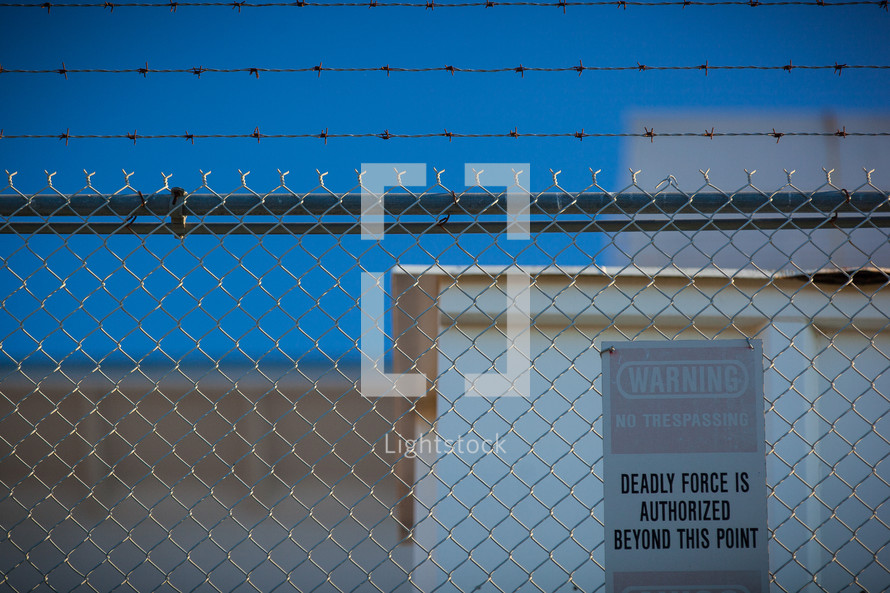 barbed wire and a chain link fence, forbidden area, deadly force authorized beyond this point, no trespassing, warning, sign