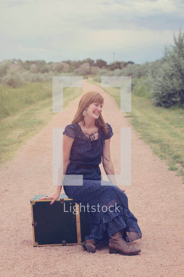 woman sitting next to luggage on a dirt road 