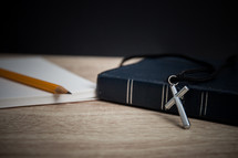 pencil, notepad, Bible, and cross necklace on a desk 